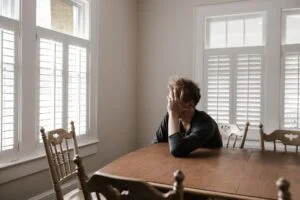 man with his head rested on his hand sitting at a wooden table