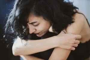 woman sitting down hugging her legs looking unhappy